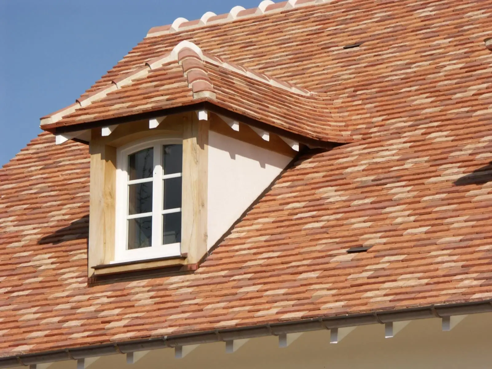 Toiture en tuiles plates avec une lucarne à fenêtre blanche.