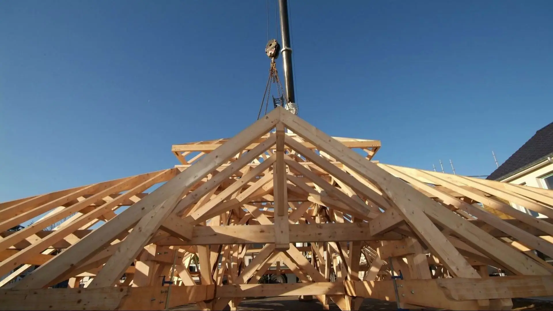Levage à la grue d’une charpente pyramidale en bois, sur fond de ciel bleu.